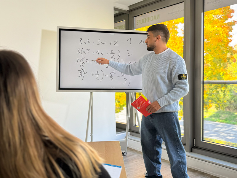 Foto vom Unterricht, Lehrer steht an der Tafel und bringt den Schüler Mathe näher
